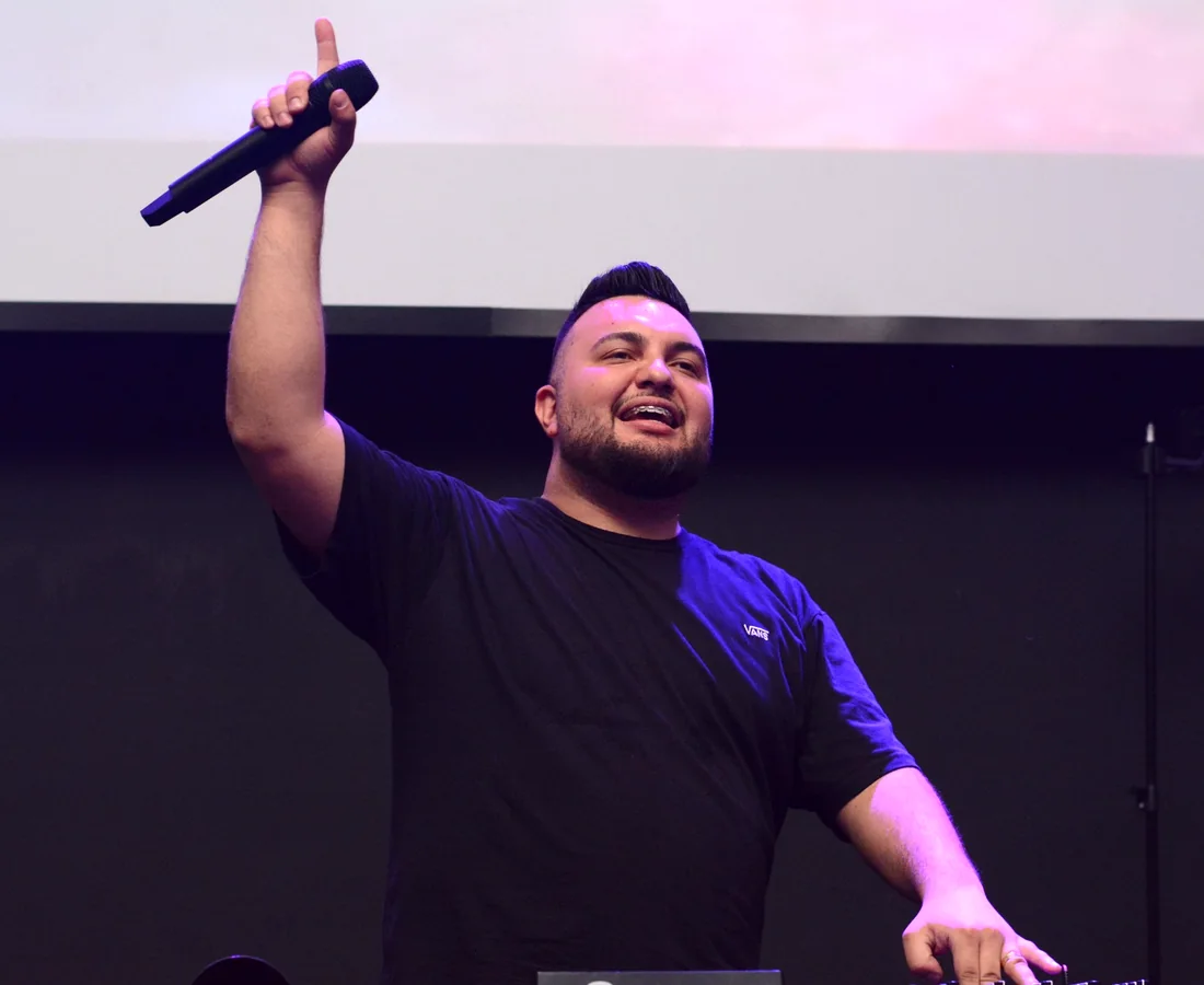DJ Vitor Capoia com microfone e braço levantado